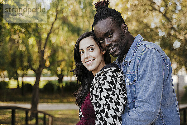 Lächelndes multiethnisches Paar  das sich im Park umarmt