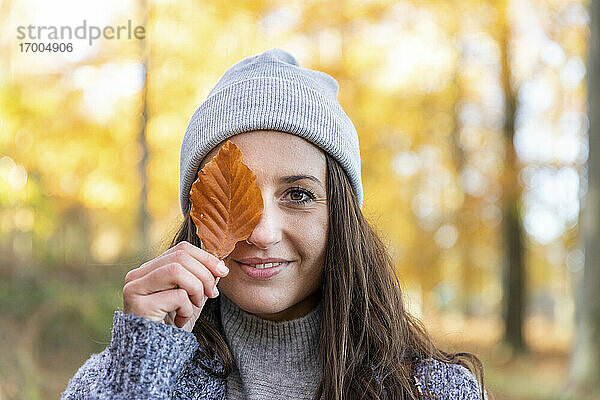 Schöne Frau bedeckt Auge mit Herbstblatt in Cannock Chase Waldgebiet