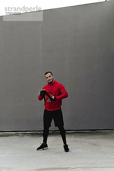 Männlicher Sportler bindet Boxband in der Hand  während er an der Wand steht