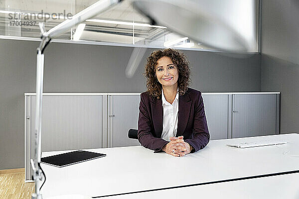 Lächelnde Geschäftsfrau sitzt am Tisch im Büro