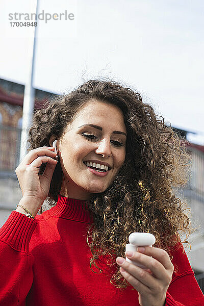 Glückliche Frau  die drahtlose In-Ear-Kopfhörer an einem sonnigen Tag anschließt