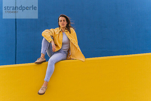 Junge Frau sitzt auf einer gelben Wand