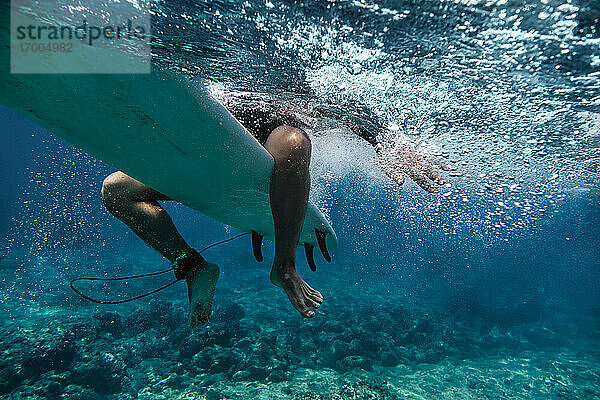 Männlicher Surfer auf dem Surfbrett sitzend beim Surfen im Meer auf den Malediven