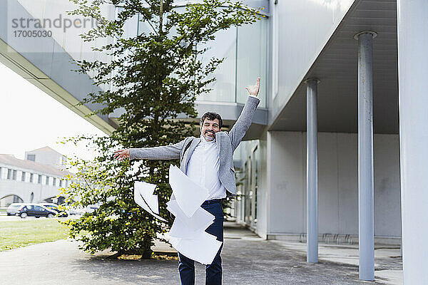 Fröhlicher Geschäftsmann wirft Dokumente  während er vor einem Bürogebäude steht