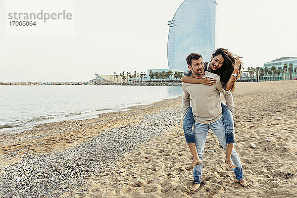 Freund nimmt seine Freundin gegen den Himmel am Strand huckepack
