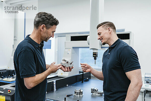 Lächelnder Techniker mit männlichem Mitarbeiter  der über ein Maschinenteil in der Industrie diskutiert