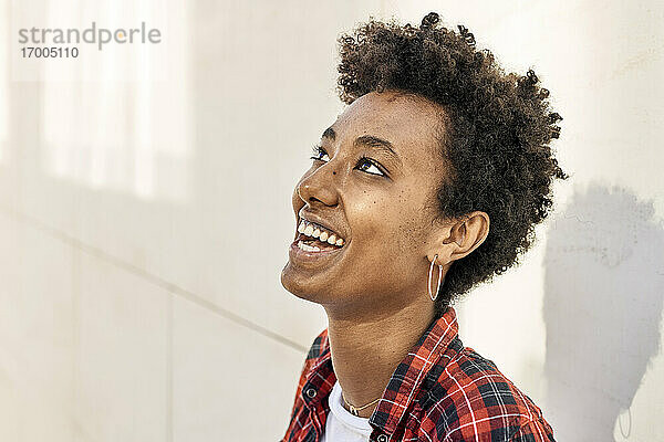 Lächelnde junge Afro-Hipsterin  die gegen eine weiße Wand blickt