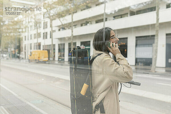 Frau mit Instrumentenkoffer  die an einer Straßenbahnhaltestelle in der Stadt mit ihrem Mobiltelefon spricht