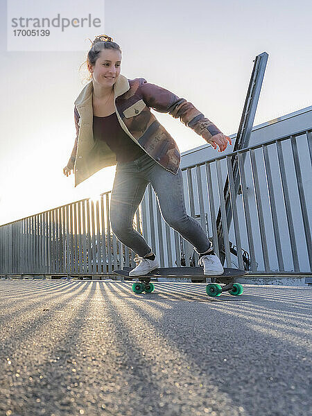 Junge Frau mit cooler Einstellung skateboarding auf Fußgängerbrücke bei Sonnenuntergang
