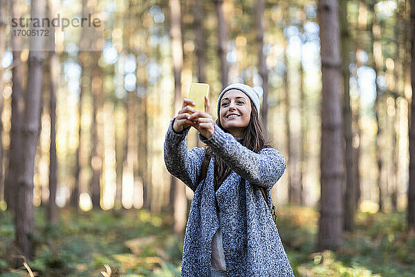 Lächelnde Wanderin  die ein Selfie mit ihrem Smartphone macht  während sie im Wald von Cannock Chase steht