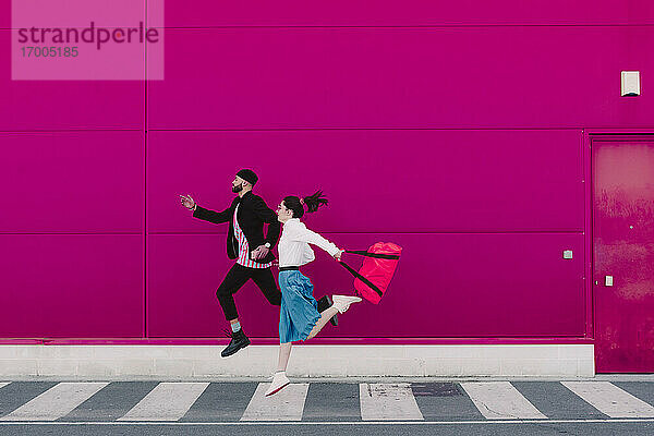 Mann und Frau laufen an einer rosa Wand entlang