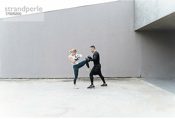Frau übt Kickboxen mit Mann  während sie an der Wand steht