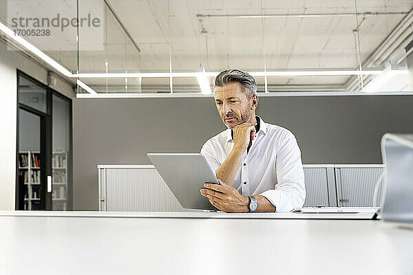 Geschäftsmann  der ein digitales Tablet benutzt  während er im Büro sitzt