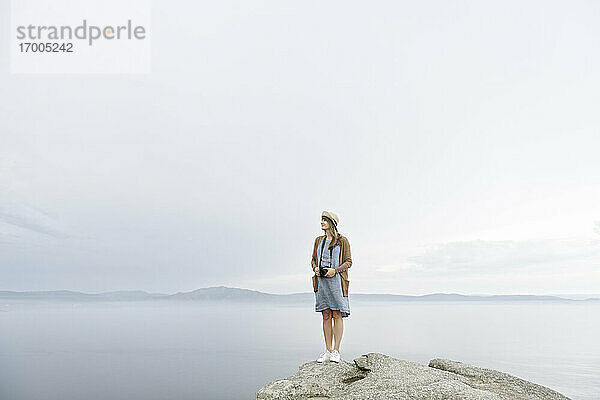 Frau mit Kamera auf einem Felsen stehend  mit Blick auf das Meer