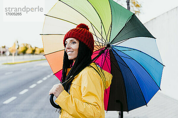 Frau hält bunten Regenschirm und schaut weg  während sie auf der Straße steht