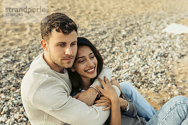 Junges Paar  das sich umarmt  während es im Sand am Strand sitzt