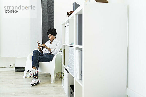 Geschäftsfrau in Bürosessel sitzend mit Smartphone in den Händen