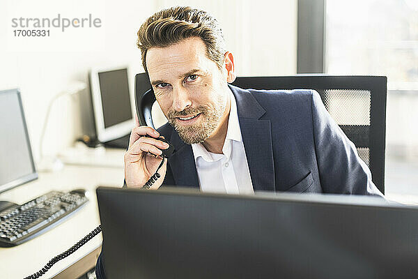 Geschäftsmann lächelnd beim Telefonieren im Büro sitzend