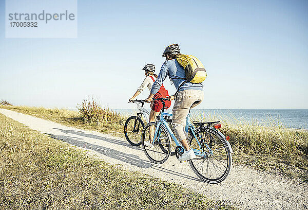 Mann mit Rucksack  der mit einer Frau auf dem Fußweg Fahrrad fährt  an einem sonnigen Tag