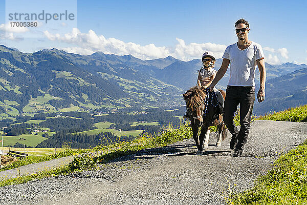 Vater geht neben seiner kleinen Tochter  die auf einem Pony reitet  einen alpinen Wanderweg entlang
