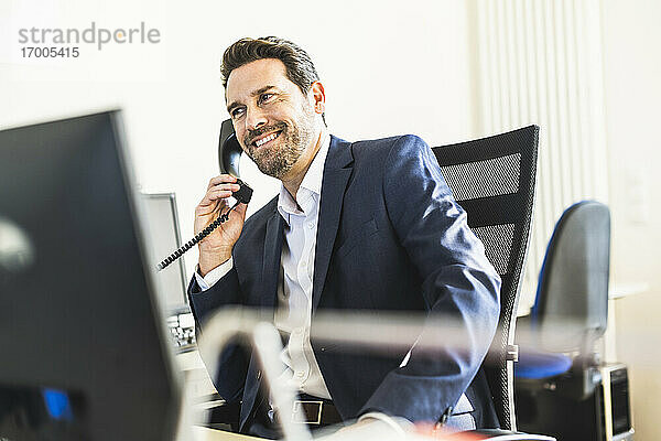 Lächelnder Geschäftsmann  der auf einem Stuhl sitzend im Büro telefoniert