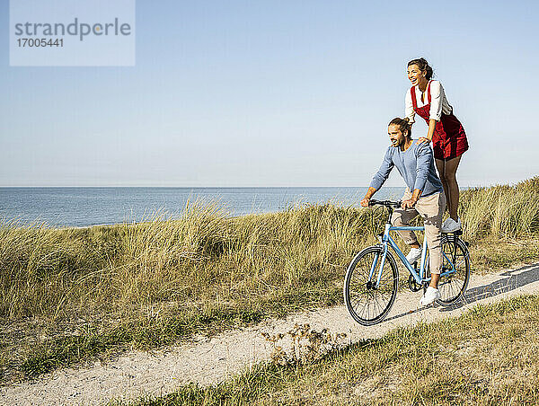 Junge Frau genießt die Fahrt mit einem Mann auf dem Fahrrad gegen den klaren Himmel