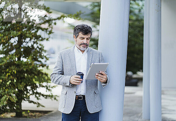 Männlicher Unternehmer  der ein digitales Tablet benutzt und eine Kaffeetasse in der Hand hält