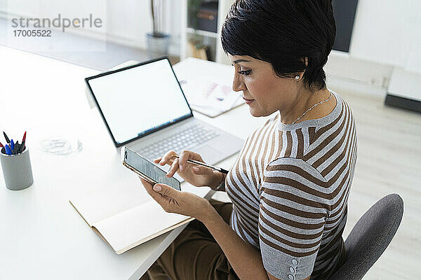 Porträt einer Geschäftsfrau  die ein Smartphone am Schreibtisch benutzt