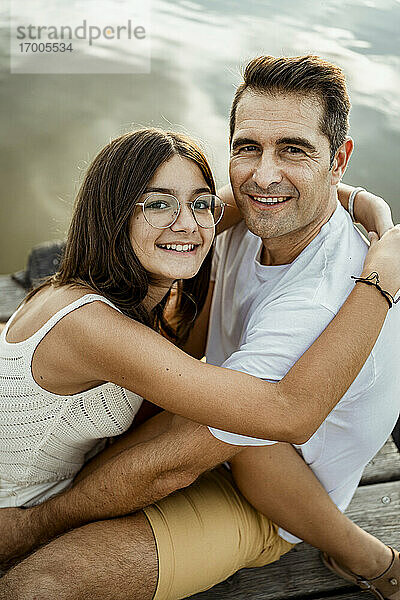 Lächelnde Tochter  die ihren Vater umarmt  während sie am Bootssteg sitzt