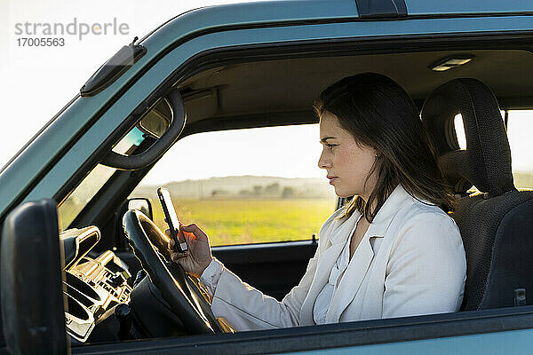 Junge Frau  die ein Mobiltelefon benutzt  während sie im Auto sitzt