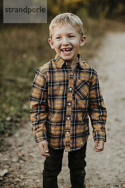 Lächelnder Junge mit kariertem Hemd auf einem Fußweg im Wald