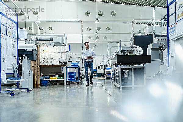 Reifer Geschäftsmann mit digitalem Tablet  der sich beim Gehen in einer Fabrik umsieht