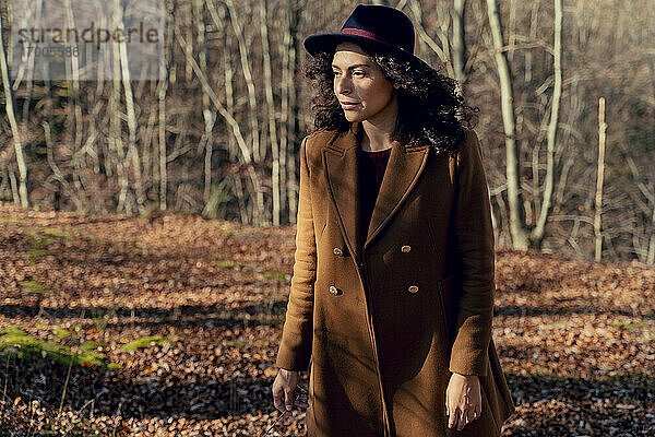 Frau mit Jacke und Hut schaut weg  während sie im Wald steht