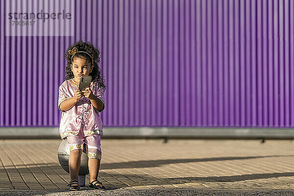 Nettes Mädchen  das einen Schmollmund macht  während es ein Mobiltelefon gegen eine lila Wand benutzt