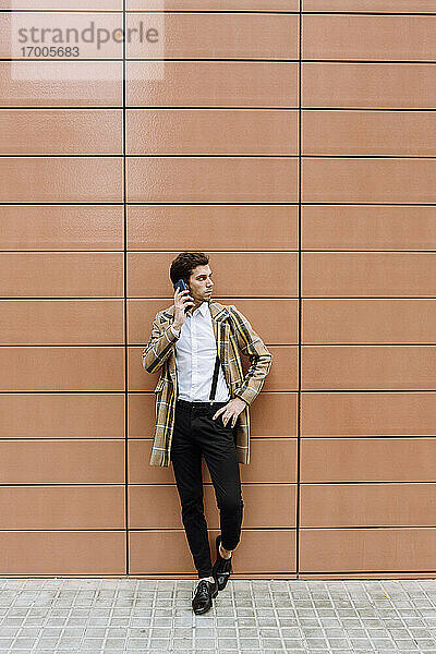 Stylischer junger Mann mit Smartphone vor einem Gebäude stehend