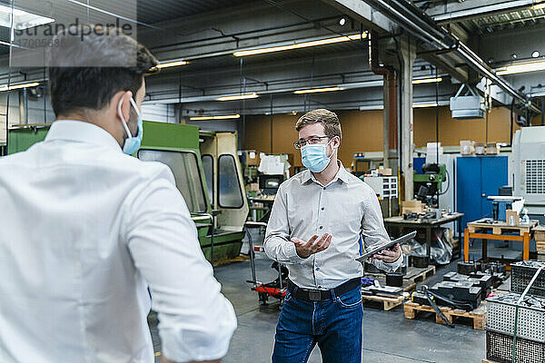 Männliche Unternehmer diskutieren mit Gesichtsschutzmaske in der Industrie