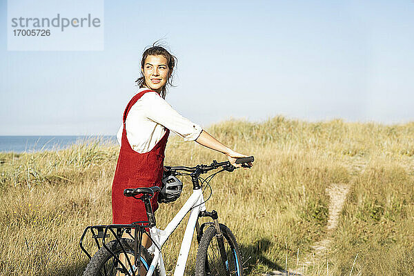 Lächelnde Frau mit Fahrrad auf dem Gehweg