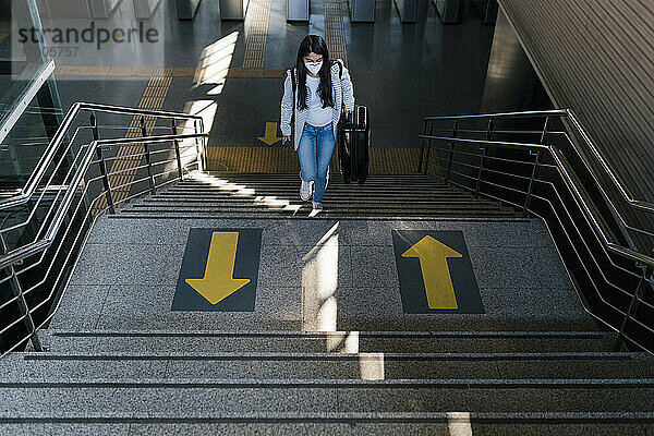 Frau mit Gepäck auf der Treppe eines Bahnhofs während einer Pandemie