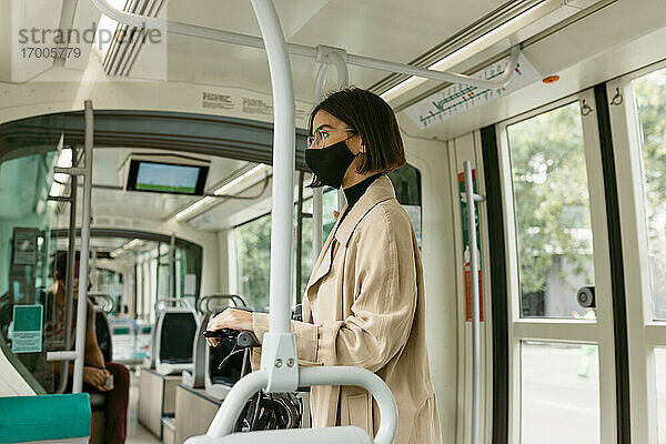 Mittlere erwachsene Frau mit Gesichtsmaske  die wegschaut  während sie mit einem Elektroroller in der Straßenbahn unterwegs ist