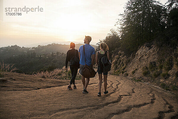 Freunde mit Tasche gehen zusammen auf einem Bergpfad bei Sonnenuntergang