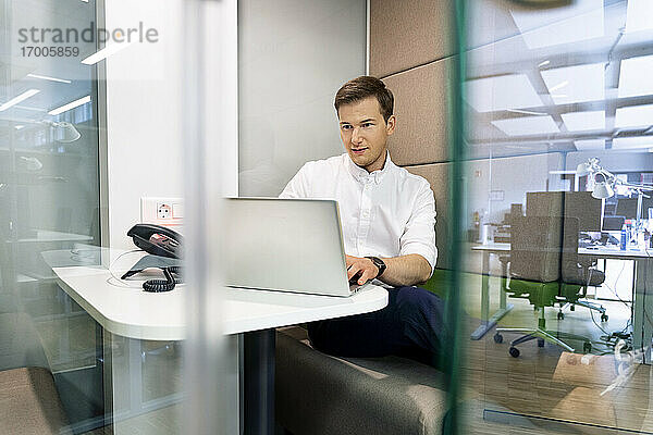 Junger Geschäftsmann arbeitet am Laptop  während er am Schreibtisch im Büro sitzt