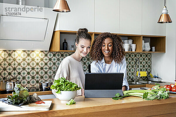 Glückliche weibliche Mitarbeiter  die sich in der Küche am Arbeitsplatz ein Rezept auf einem Tablet ansehen