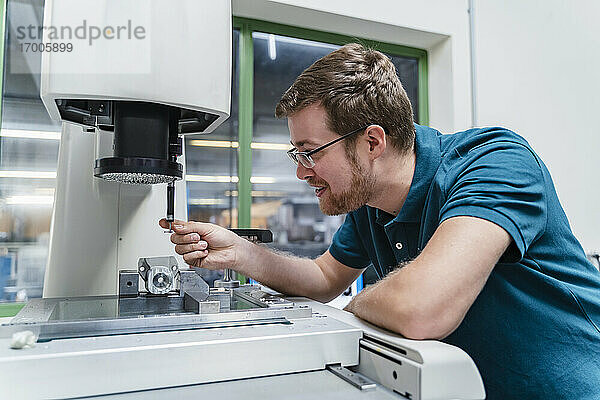 Lächelnder männlicher Fabrikarbeiter  der eine Vermessungsmaschine in der Industrie analysiert