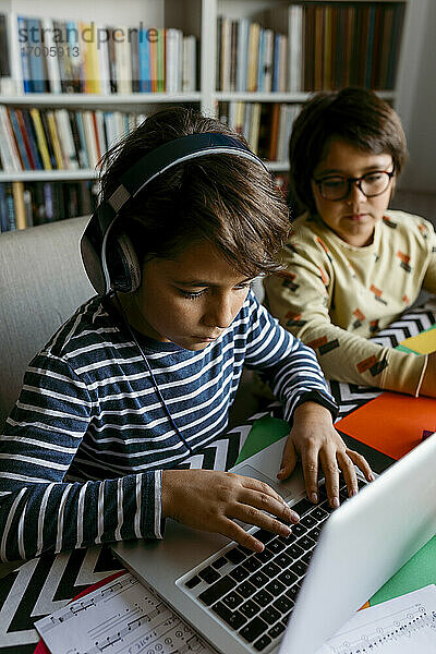 Junge mit Laptop beim E-Learning mit einem männlichen Freund zu Hause sitzend