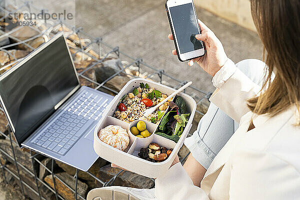 Unternehmerin mit Smartphone und wiederverwendbarer Lunchbox in der Hand