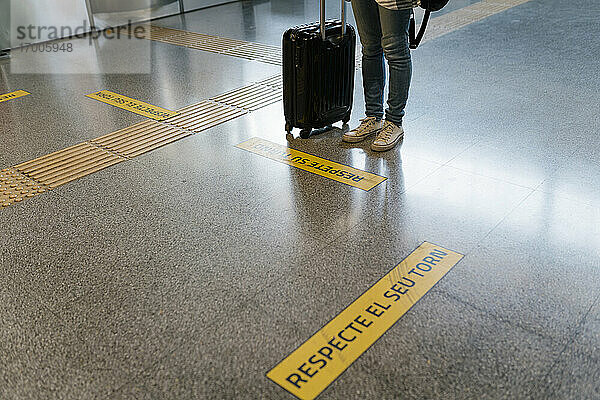 Frau mit Gepäck  die mit einem Schild auf dem Boden einer U-Bahn-Station auf ihren Einsatz wartet