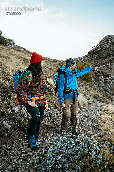 Mittlerer erwachsener Mann  der beim Wandern mit seiner Freundin auf einem felsigen Berg im Urlaub auf etwas zeigt