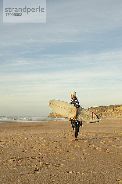 Mittlerer erwachsener männlicher Surfer mit Surfbrett am Strand gegen den Himmel