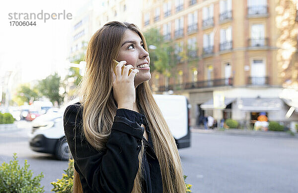 Junge Frau  die auf der Straße in der Stadt steht und mit ihrem Handy telefoniert
