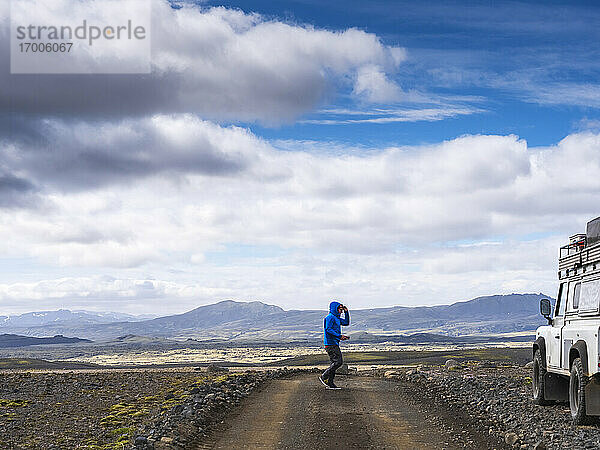 Männlicher Tourist  der auf einer unbefestigten Straße in Richtung Geländewagen gegen den Himmel läuft  Lakagigar  Island